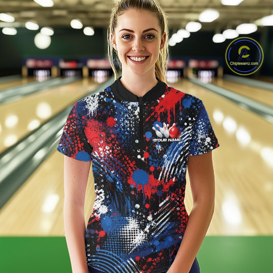 A woman stands in a bowling alley wearing a custom short-sleeve quarter zip with red, blue, white, and black paint-splatter graphic