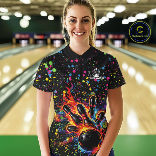 Female model wearing a black bowling quarter-zip shirt at the bowling lane with colorful paint splatters and bowling strike graphics.