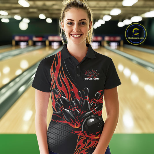 Female model seen from the front in a bowling lane wearing a black polo shirt featuring a red flaming black bowling ball striking pins in a dynamic action scene.