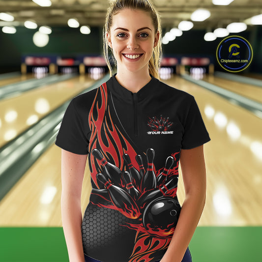 Female model front view inside bowling center wearing black quarter zip shirt featuring red flame bowling ball knocking down pins artwork