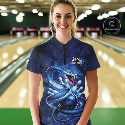 Female model wearing a bowling quarter-zip in a bowling lane with blue cobra artwork wrapped around a bowling ball and scattered pins.