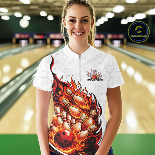 Front view female model at bowling lane wearing white and red quarter zip shirt showing flaming bowling ball crashing into pins with energetic fire illustration.
