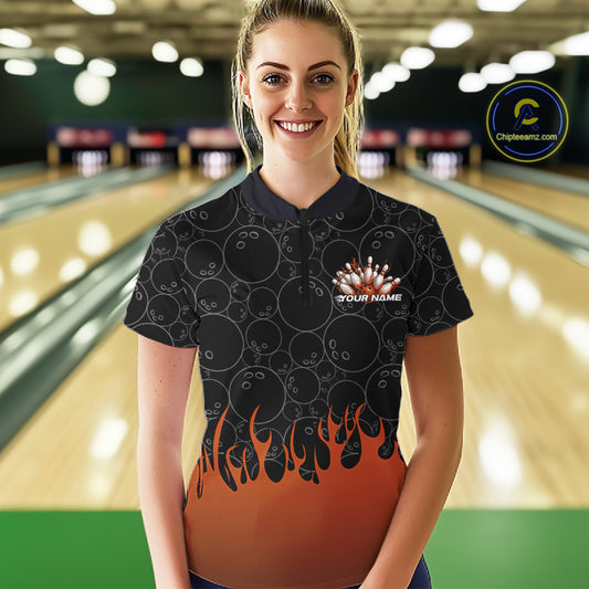 In a bowling lane, front view of a female model wearing a black bowling quarter-zip shirt with vibrant orange flames, featuring flaming bowling ball striking pins illustration.