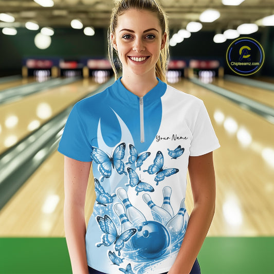 Female model wearing a white and blue bowling quarter zip with butterfly artwork and bowling graphics, front view inside a bowling alley
