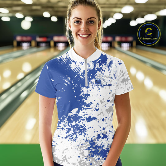 Front view of a female model in a bowling lane wearing a bowling quarter-zip shirt with blue and white splatter background and clean sporty bowling-inspired graphics.