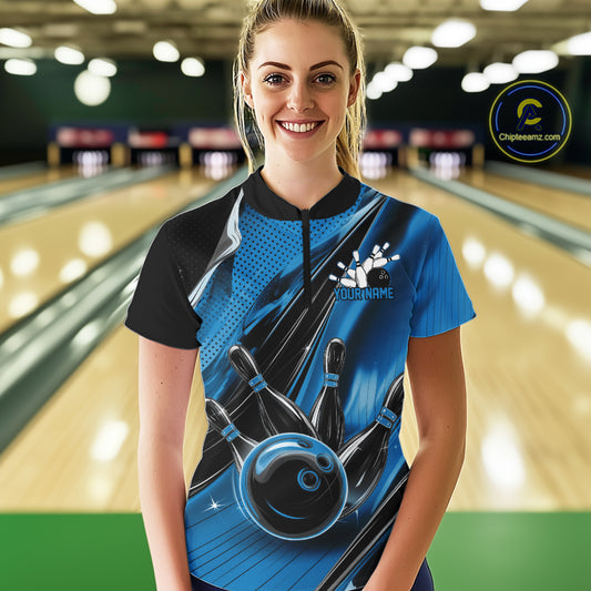Female model wearing a black and blue bowling quarter-zip shirt at the bowling lane with energetic bowling strike artwork and motion streaks.