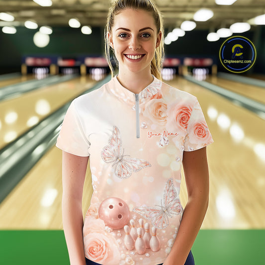 Female model at a bowling lane wearing a quarter-zip bowling shirt with pastel glitter butterflies floating above bowling pins and a bowling ball.