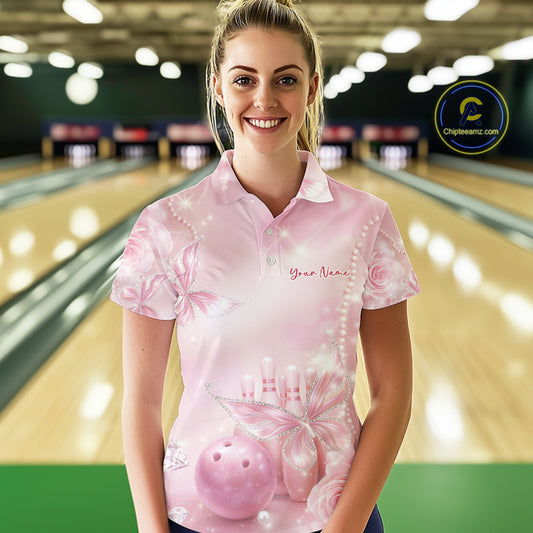 Female model wearing a bowling polo shirt in a bowling center with pink glitter butterflies, diamonds, bowling pins, and bowling-themed artwork.