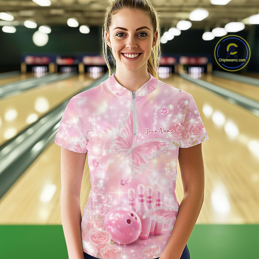 Female model at a bowling lane wearing a quarter-zip bowling shirt with glitter butterfly graphics, diamond accents, bowling pins, and a bowling ball.