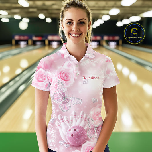 Female model wearing a bowling polo shirt in a bowling alley with pink glitter butterflies, floral rose accents, bowling pins, and a bowling ball.
