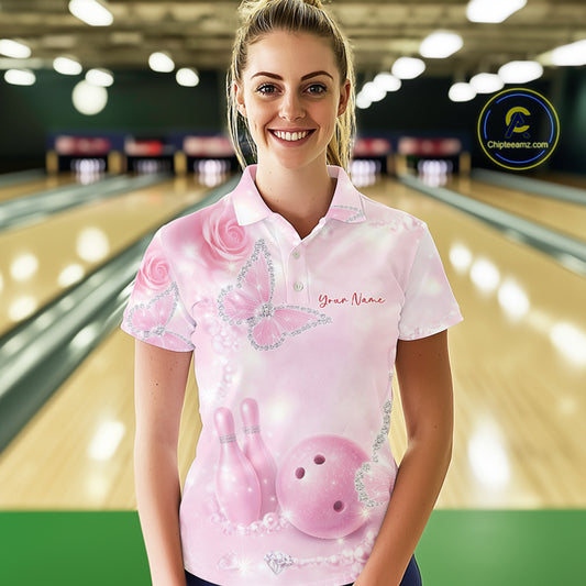Female model wearing a bowling polo shirt at a bowling lane with pink glitter butterflies, roses, bowling pins, and bowling ball artwork.