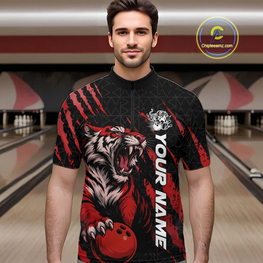 Front view of a male model at a bowling lane wearing a black and red bowling quarter-zip shirt featuring a roaring tiger holding a red bowling ball with matching red claw-stripe artwork and a geometric background pattern.