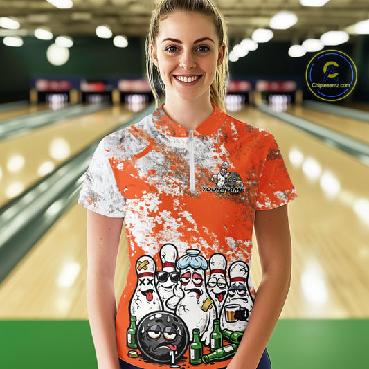 Front view of a female model in a bowling lane wearing an orange and white grunge splatter bowling quarter-zip shirt with playful bowling pins and beer bottle graphics.