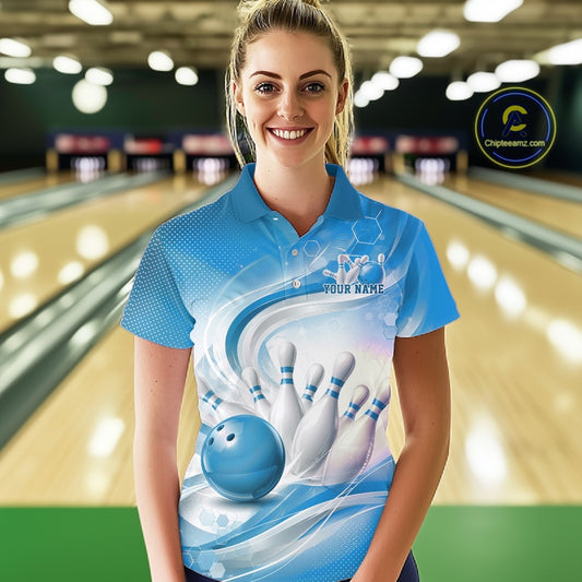 Female model standing in a bowling lane wearing a white and blue bowling polo shirt featuring abstract wave lines and a glossy bowling ball striking pins on the front.