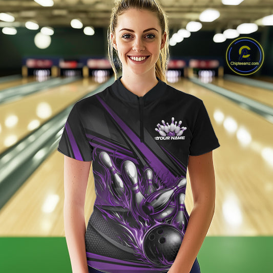Female model in a bowling lane wearing a black quarter-zip shirt, purple flame bowling ball hitting pins with modern abstract stripe graphics.