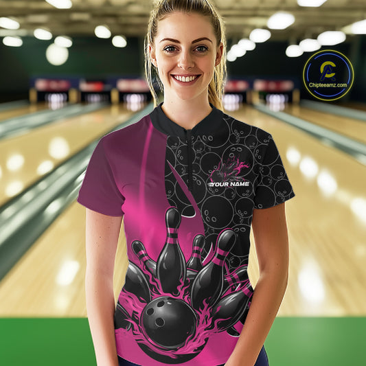 Female model in a bowling lane wearing black and pink quarter zip shirt, front view featuring flaming bowling ball striking pins dynamic sports design