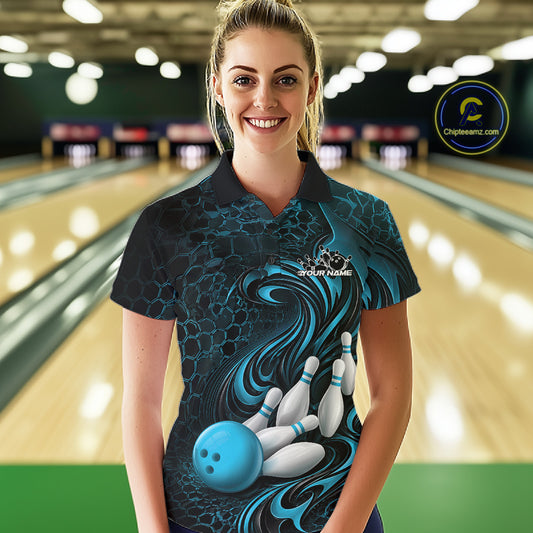 Female model standing in a bowling lane wearing a black and blue bowling polo shirt featuring a tribal flame bowling ball and pins graphic on the front.