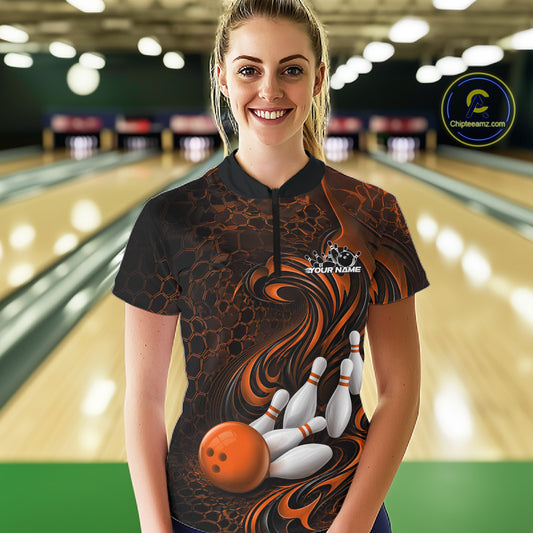 Female model standing in a bowling lane wearing a black and orange bowling quarter-zip shirt featuring a tribal flame bowling ball and pins graphic on the front.