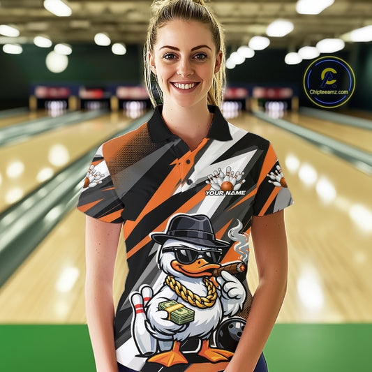 Female model wearing a black and orange bowling polo at the bowling lane with duck artwork in sunglasses and fedora holding cash and a cigar beside bowling pins.