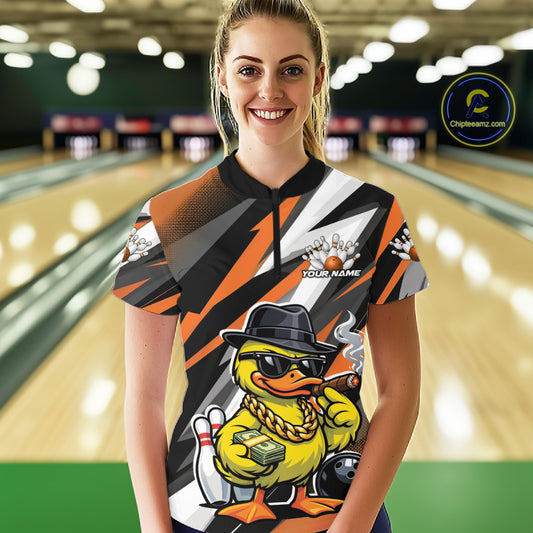 Front view female model at bowling lane wearing black and orange quarter zip shirt showcasing duck in sunglasses and fedora with bowling ball and pins illustration.