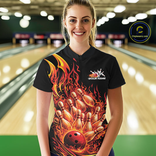 Front view female model at bowling lane wearing black and red quarter zip shirt with flaming bowling ball striking pins and bold fire themed illustration.