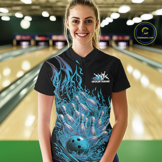 Front view female model at bowling lane wearing black and blue quarter zip shirt displaying flaming bowling ball striking pins with energetic fire burst illustration.