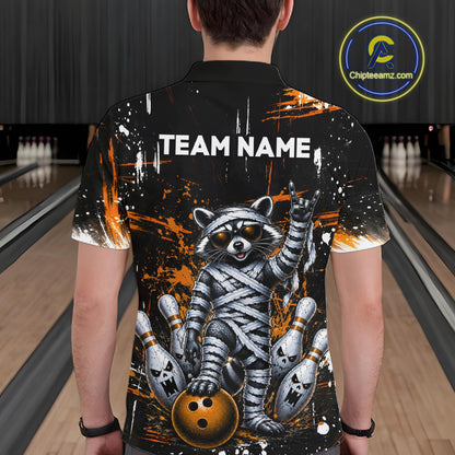 A person viewed from behind wearing a black short-sleeve bowling-themed graphic shirt with a mummy raccoon, bowling pins, and orange paint splatter design. The shirt has 'TEAM NAME' printed across the upper back.