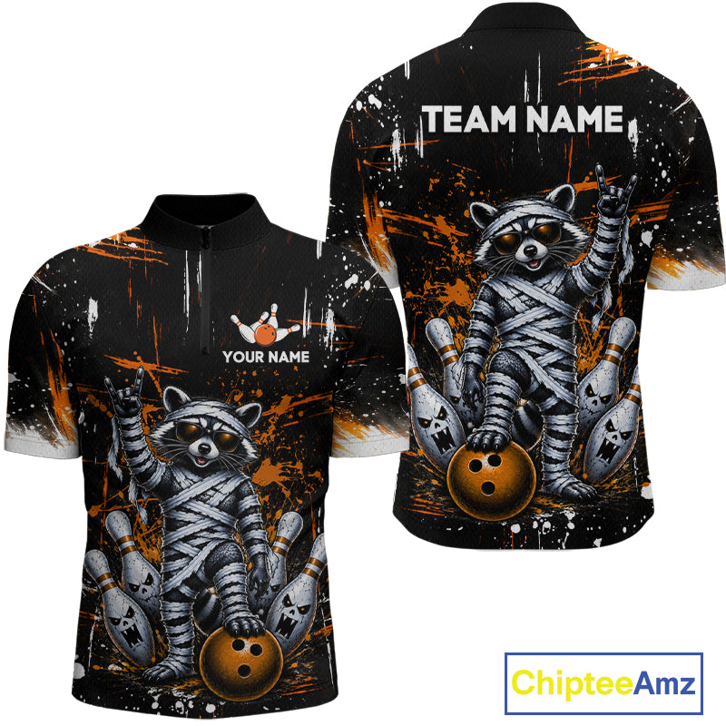 Front and back views of a short-sleeve athletic jersey with a raccoon mummy graphic holding bowling pins and a bowling ball, on a black background with orange paint splatter. The front has placeholder text 'YOUR NAME' and 'TEAM NAME' on the back.