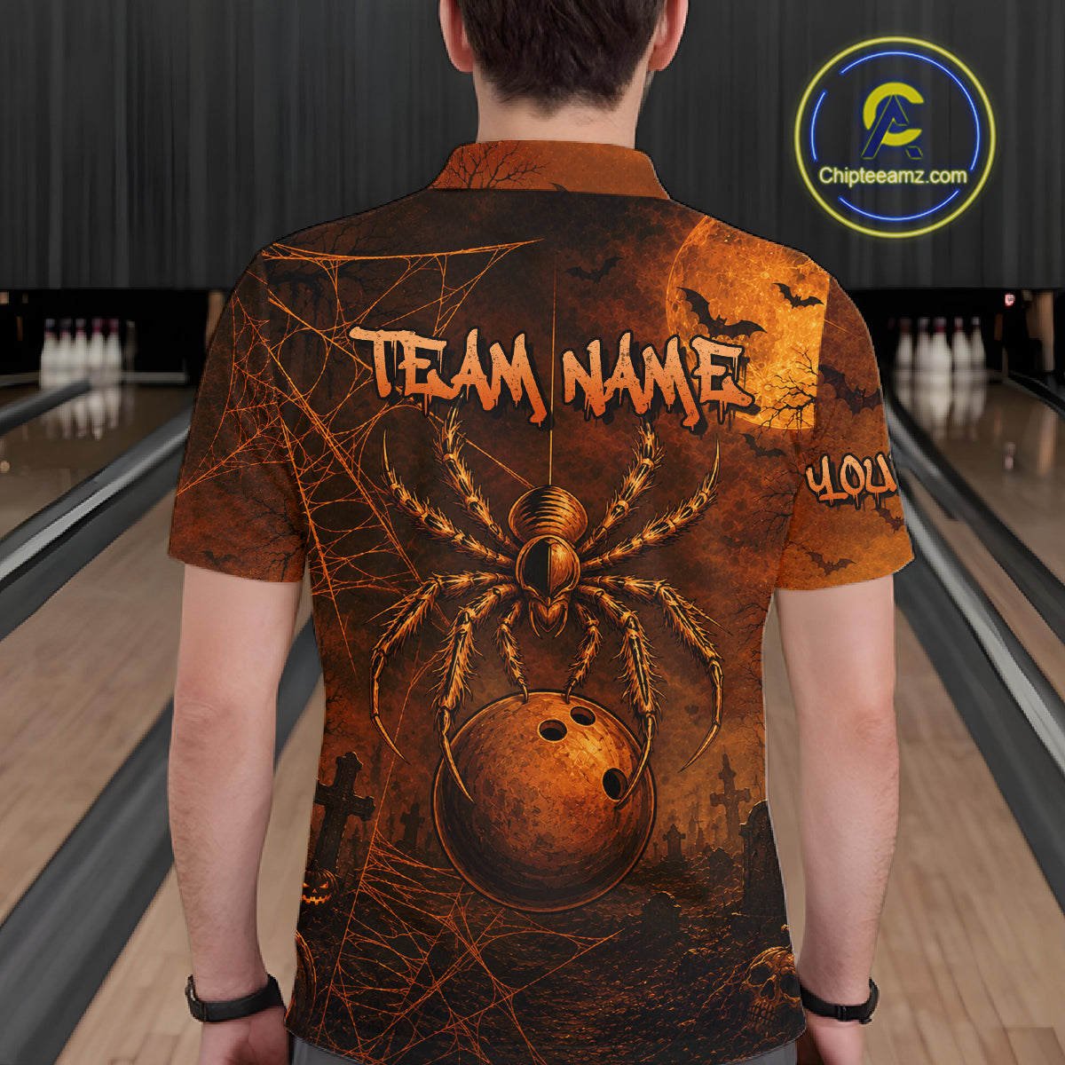 A man viewed from behind wearing a short-sleeve bowling shirt with a spooky Halloween graphic featuring a large spider, a bowling ball, bats. The background shows blurred bowling lanes.