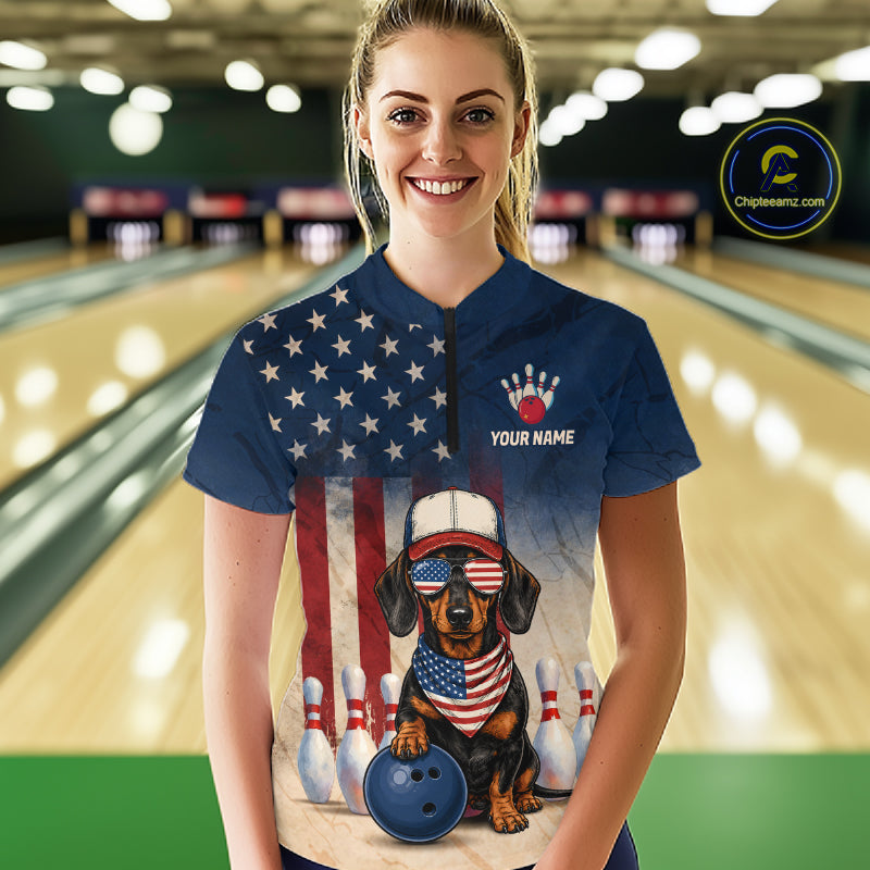 Person wearing a blue t-shirt with a dog design and American flag, standing in a bowling alley.