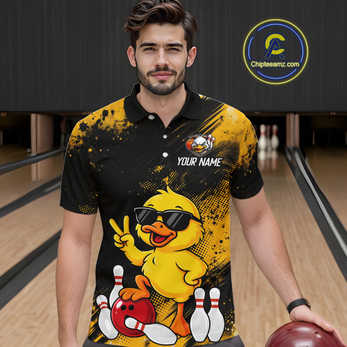 A man wearing a black and yellow bowling-themed custom polo shirt with a cartoon duck graphic, standing in a bowling alley. The shirt features a yellow duck wearing sunglasses, bowling pins, and a red bowling ball, with 'YOUR NAME' printed on the chest.