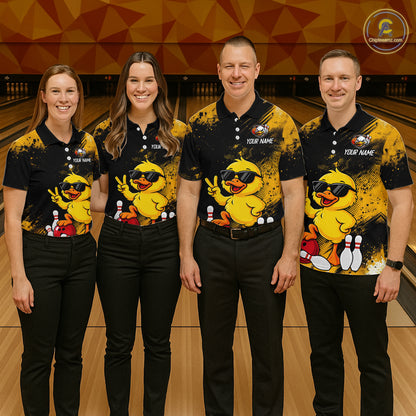 Four people standing together in a bowling alley wearing matching black and yellow bowling shirts with a cartoon duck graphic, black pants, and bowling pins visible in the background.