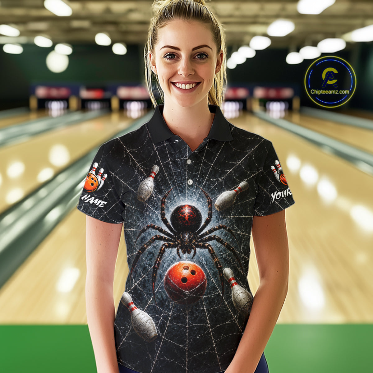 A woman standing in a bowling alley wearing a black short-sleeve polo shirt with a large spider and bowling ball graphic on the front, with bowling pins and lanes blurred in the background.