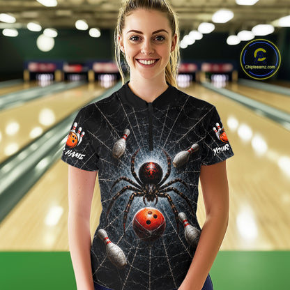 A woman standing in a bowling alley wearing a black short-sleeve bowling-themed t-shirt with a large spider and bowling ball graphic on the front, with bowling pins and lanes visible in the background.