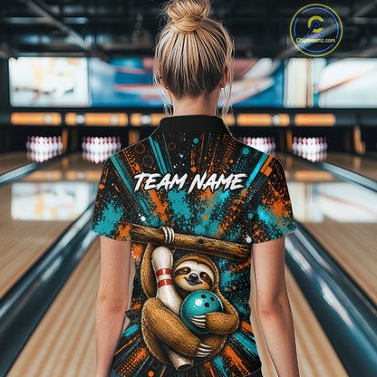 A woman viewed from behind in a bowling alley, wearing a short-sleeve collared shirt with a large back graphic. The shirt has a black base with teal and orange paint-splatter style artwork, a sloth holding bowling pins and a teal bowling ball, and the text 'TEAM NAME' across the upper back.