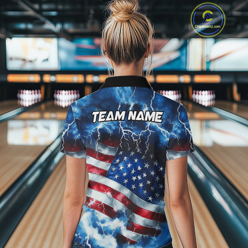 A woman viewed from behind wearing a short-sleeve collared shirt with a patriotic American flag design featuring lightning and the text 'TEAM NAME' on the back, standing in a bowling alley.