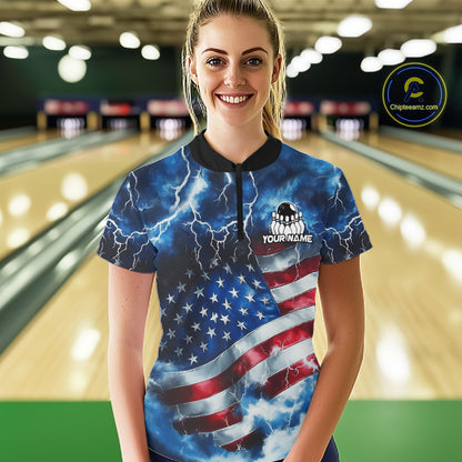A woman stands in a bowling alley wearing a short-sleeve collared shirt with a blue, white, and red lightning-and-flag print. The shirt has a black collar and a small chest graphic that reads 'YOUR NAME' with a bowling pin icon.