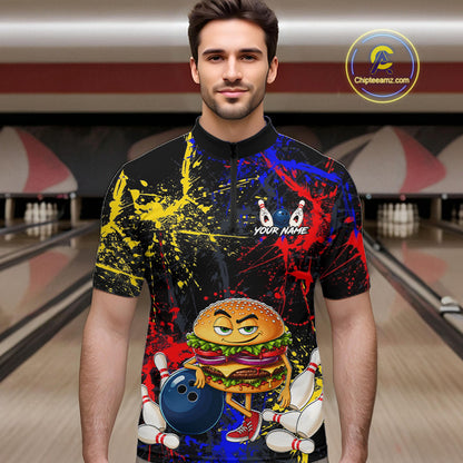 A man wearing a short-sleeve black bowling-themed t-shirt with a colorful paint splatter design and a cartoon burger character holding a bowling ball. The background shows a blurred bowling alley.