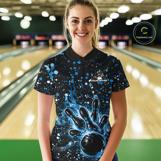Female model in a black bowling quarter-zip shirt at the lane featuring blue paint splatter accents and bowling strike artwork.