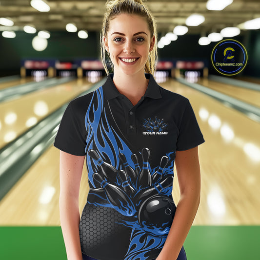 Female model seen from the front in a bowling lane wearing a black polo shirt featuring a blue flaming black bowling ball striking pins in a dynamic sports action design.