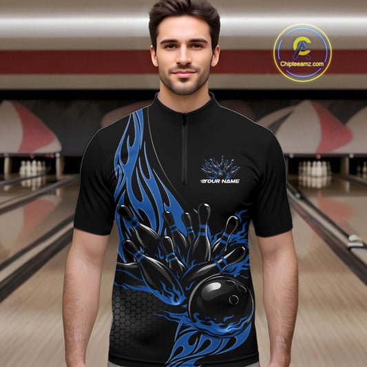 Male model seen front view inside bowling center wearing black quarter zip shirt with blue flaming bowling ball knocking down pins in vivid motion scene.