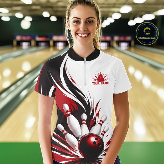 Front view of a female model wearing a white, black, and red bowling quarter zip shirt with a flaming bowling ball and pins illustration at a bowling lane.