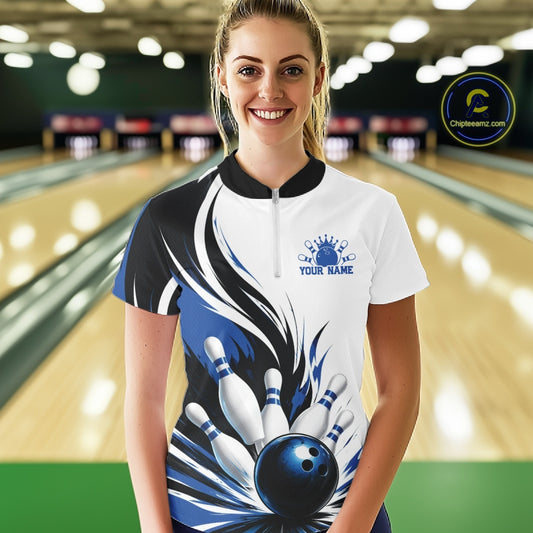 Female model wearing a white, black, and blue bowling quarter zip shirt featuring a flaming bowling ball hitting the pins, shown from the front in a bowling lane.