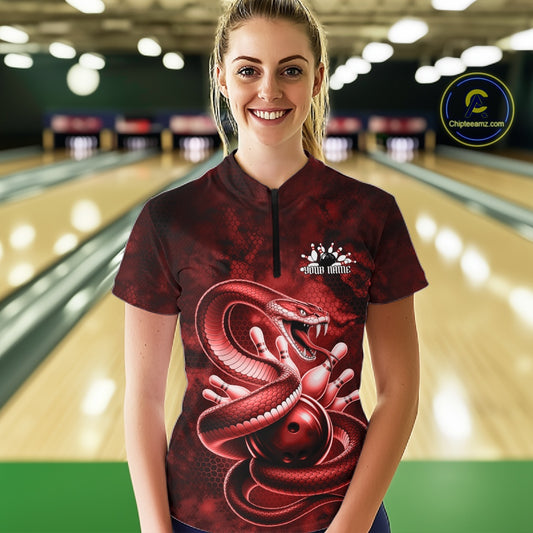 Female model at the bowling lane wearing a quarter-zip with red cobra artwork wrapped around a bowling ball.