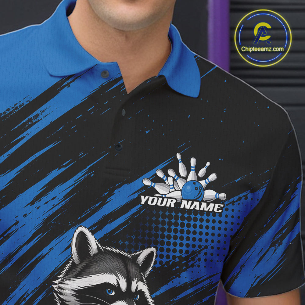 A close-up of a person wearing a custom bowling-themed polo shirt. The shirt features a black and blue brushstroke pattern, a raccoon graphic, and a bowling pin/ball graphic with the text 'YOUR NAME'.