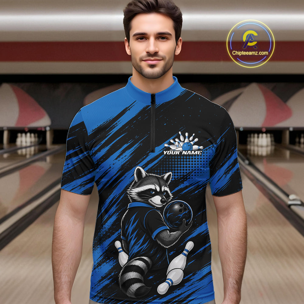 A man wearing a short-sleeve bowling-themed quarter-zip shirt with a raccoon graphic and blue/black brushstroke pattern, standing in front of a bowling alley background.