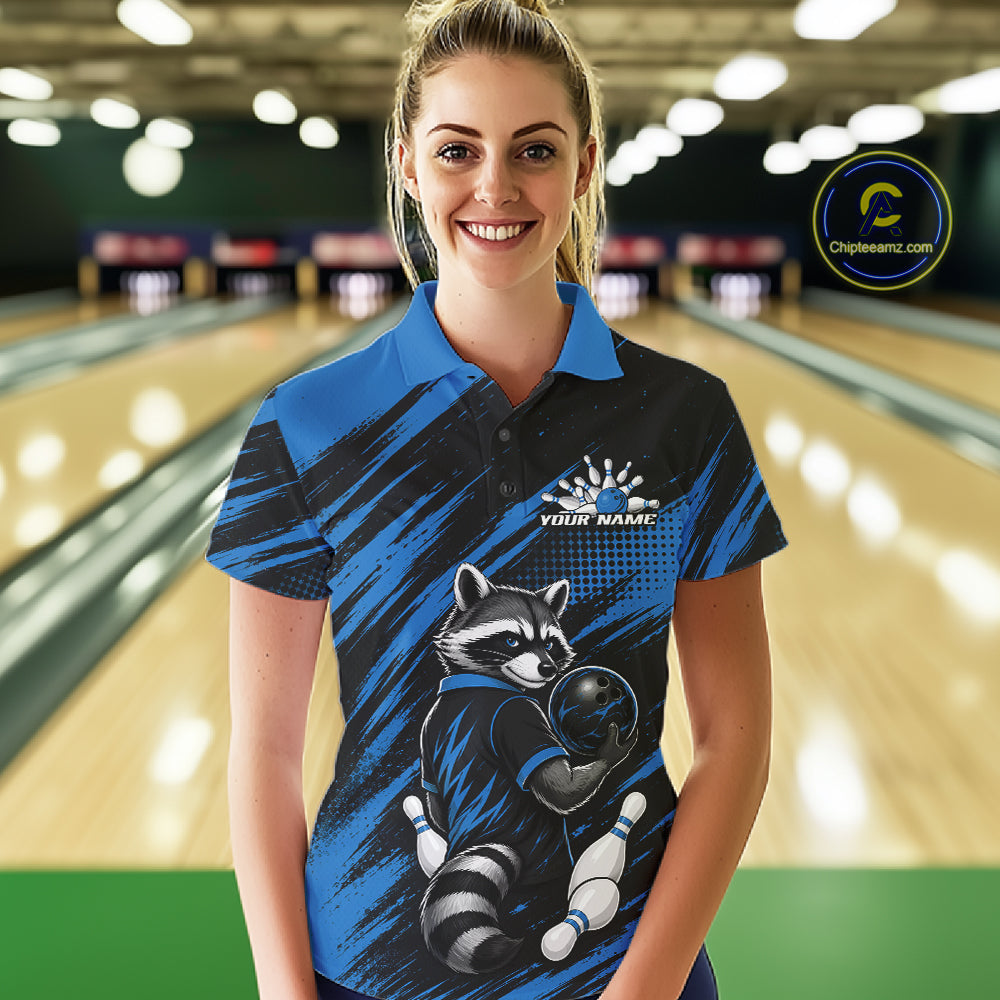 A woman stands in a bowling alley wearing a custom blue and black short-sleeve bowling quarter zip shirt with a raccoon graphic and 'YOUR NAME' printed on the chest. 