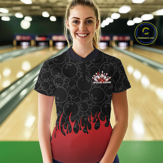 Front view of a female model at a bowling lane wearing a black quarter-zip shirt with vibrant red flames and bowling ball pattern creating a powerful bowling strike scene.