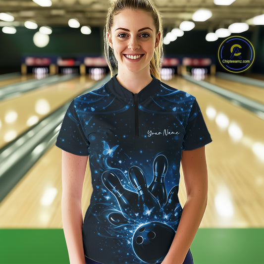 Female model wearing a black and blue bowling quarter-zip shirt featuring glowing butterfly accents and bowling graphics inside a bowling center.