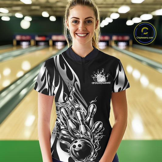 Female model front view at bowling lane wearing black quarter zip shirt with silver metal tribal flame bowling ball hitting pins design